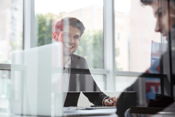 Two cheerful young businessmen with laptop on business meeting in office